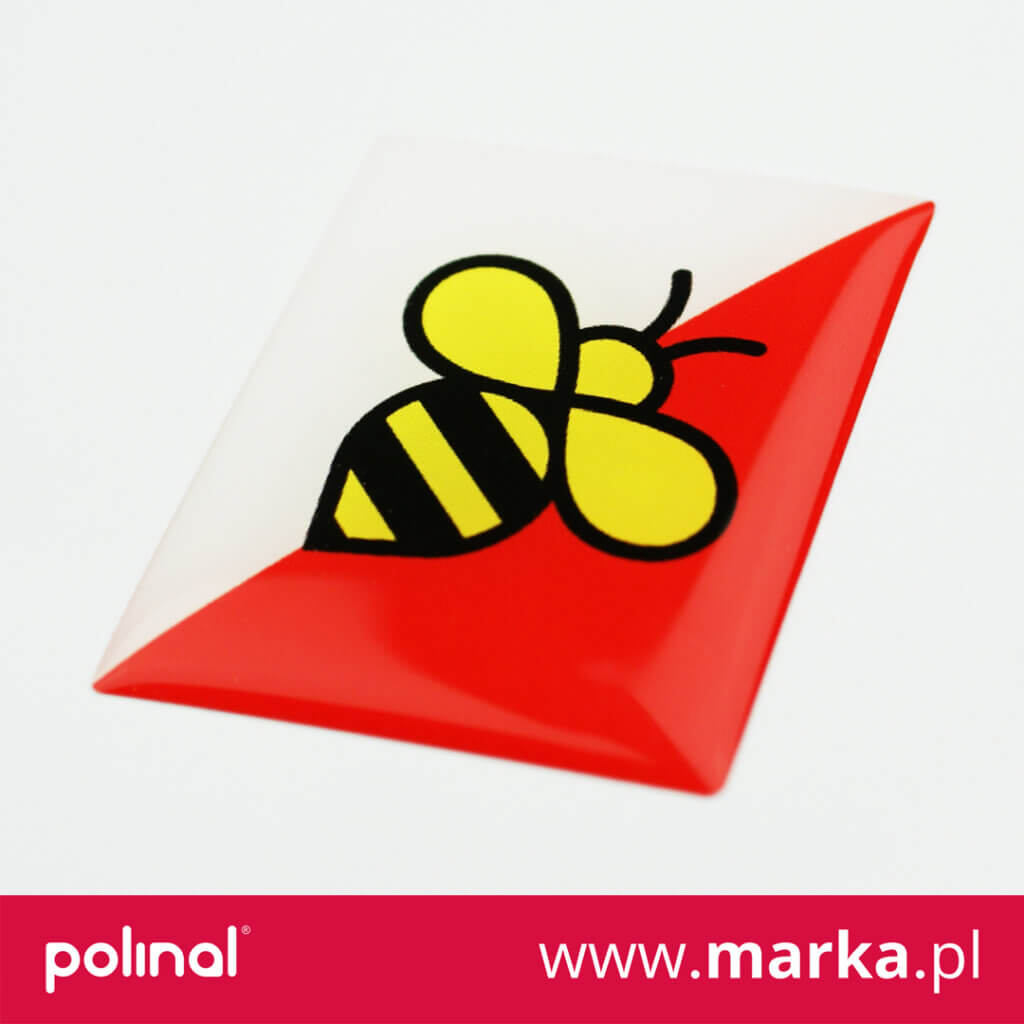 Biało-czerwona naklejka z nadrukiem logo pszczoły narysowane grubą czarną kreską, z wnętrzem wypełnionym kolorem żółtym.  