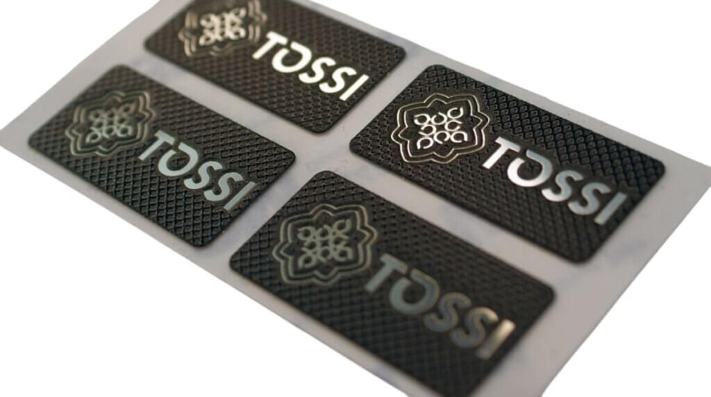 Four black plates with the silver logo of the furniture manufacturer TOSSI