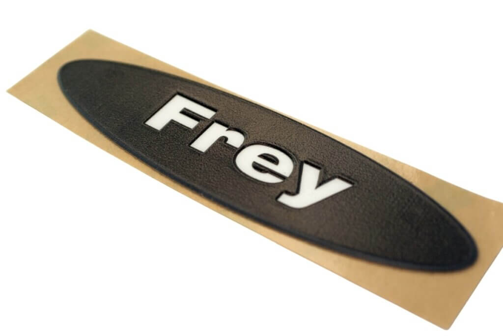 owalny czarny emblemat z logo firmowym logo białym napisem Frey