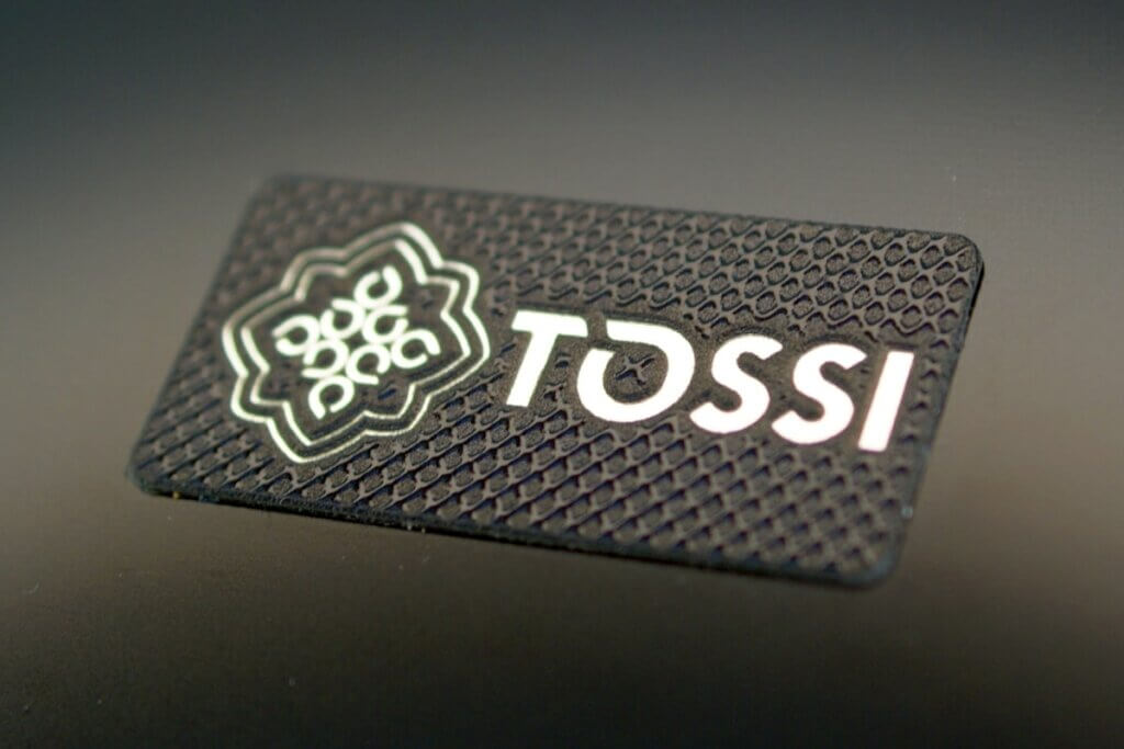 Black rectangular branding plate with the TOSSI logo